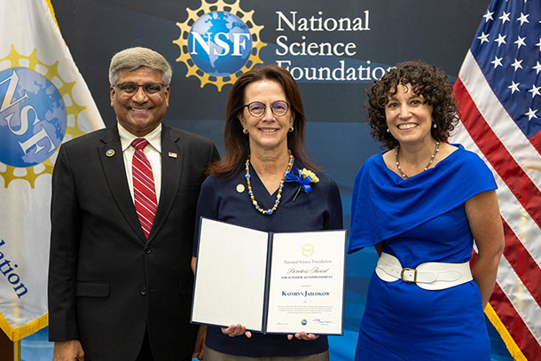 Three people pose for a photo with the person in the center holding an award.