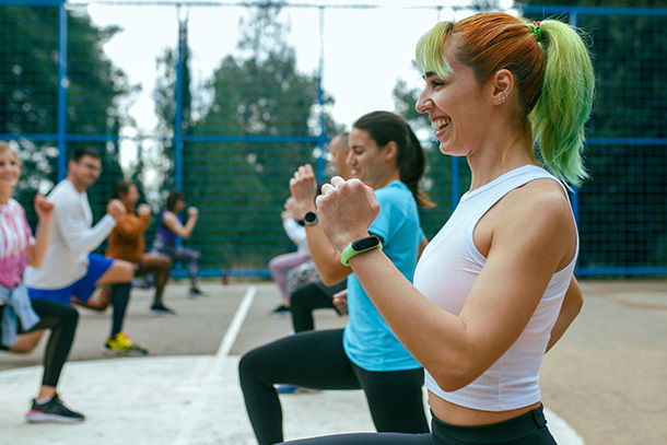 people in workout gear and fitness trackers perform lunges in exercise class on outdoor tennis court