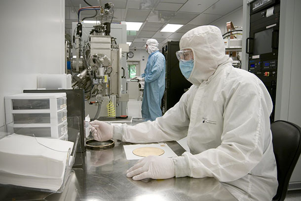 A person in a white lab suit and blue face mask works in a lab