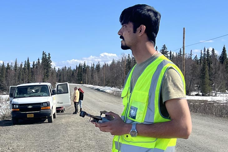 person in safety vest operates a remote control along a country road
