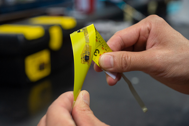 Two hands are pictured twisting a yellow electronic that resembles a tape measure. 