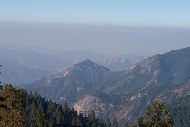 smog hovers over a range of pine tree-covered mountains