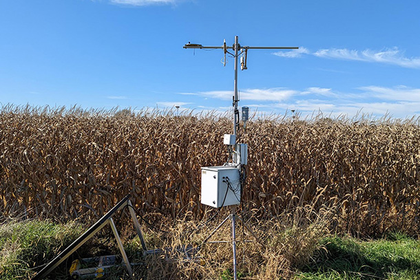 tripod with white metal box stands in front of cornfield of dried cornstalks