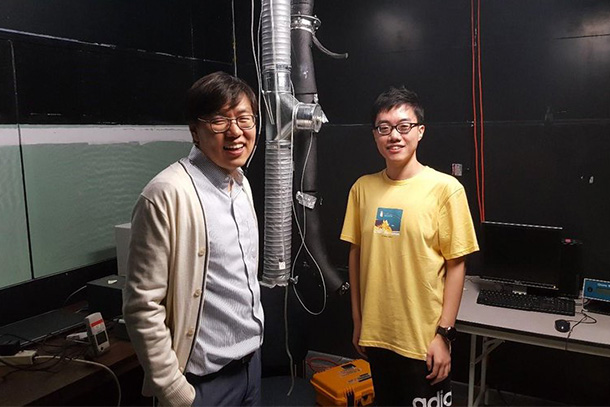 Two people wearing glasses pose near research laboratory equipment.