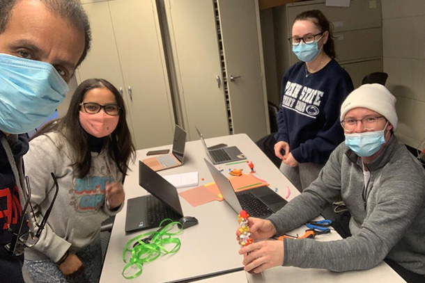 A group of students wearing masks sits around a lab table