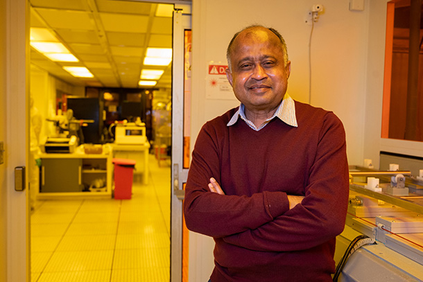Madhavan Swaminathan stands and smiles at the camera. Lab equipment is visible in the background. 
