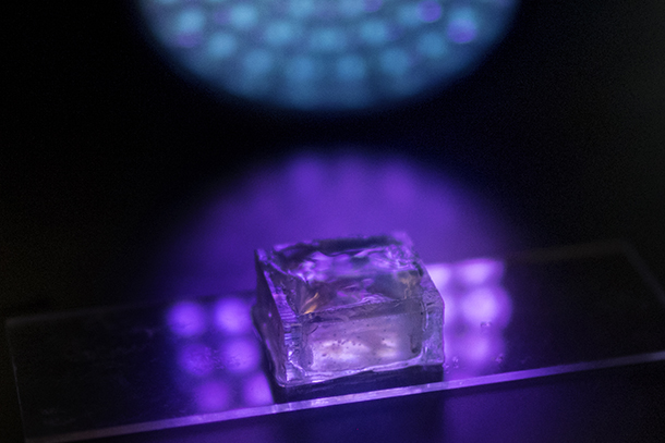 A transparent cube sits on a transparent slide, a purple glow encompassing both objects. 