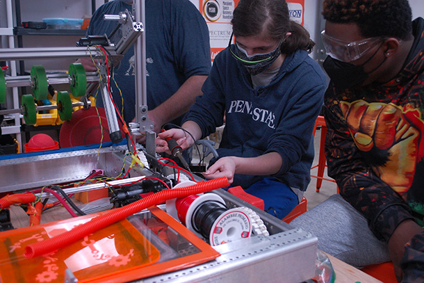 Two people wearing masks use soldering equipment
