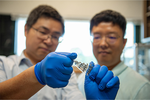 Two researchers wearing blue gloves twist a stretchy transistor