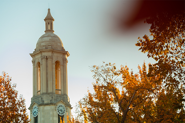 The top of Old Main at Penn State University Park with fall leaves visible in the foreground. 