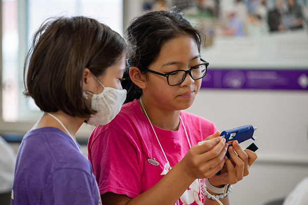 Two students stand together preparing a hot glue gun for use. 