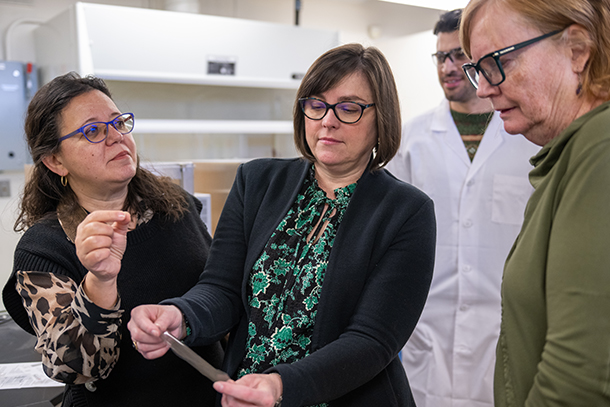 Three female researchers wearing business attire examine material in lab setting. 