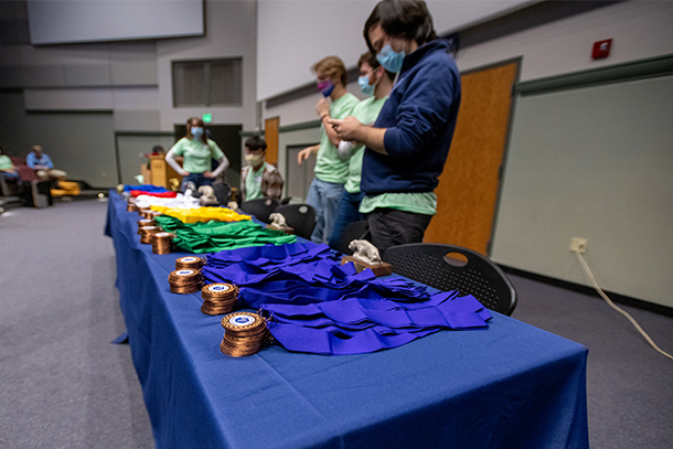 Five college students stand behind a table with piles of medals and trophies on it