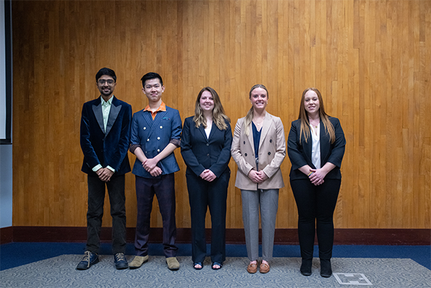 Five individuals wearing professional attire pose indoors