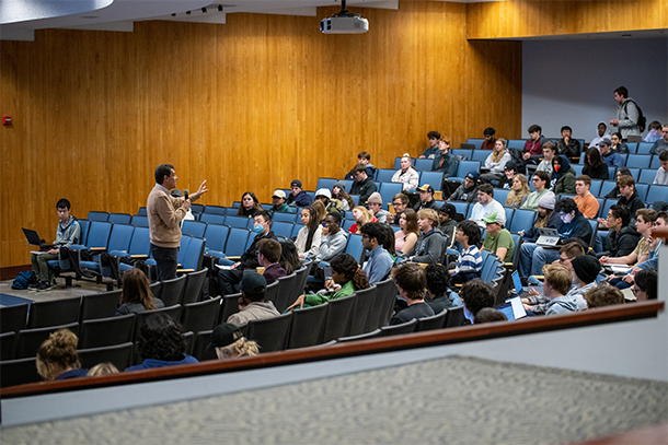 A crowd of students sit in an auditorium and listen to student presentations