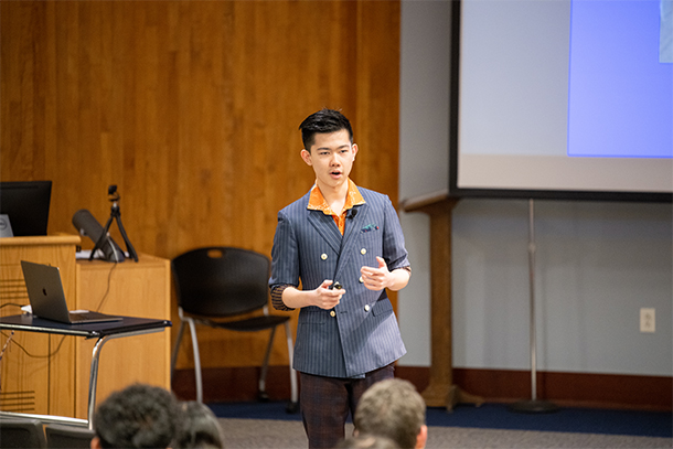 An individual holding a clicker presents to an auditorium of students