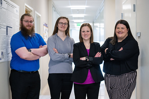 Four people stand in a hallway, facing the camera.