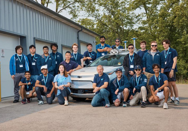 Team members pose for a picture with their autonomous vehicle in front of a garage. 