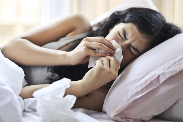 An individual blowing her nose in bed.