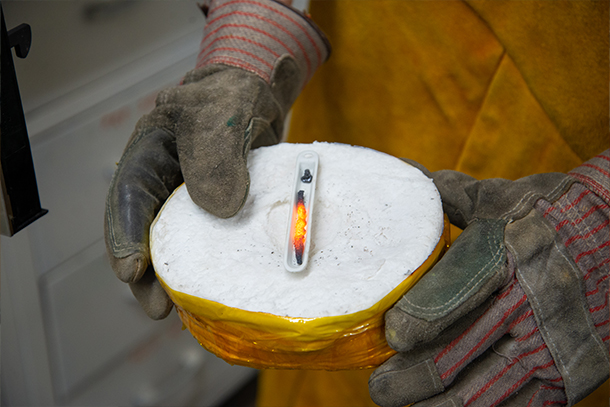 An individual holds a sample of red hot metal in a small circular chamber
