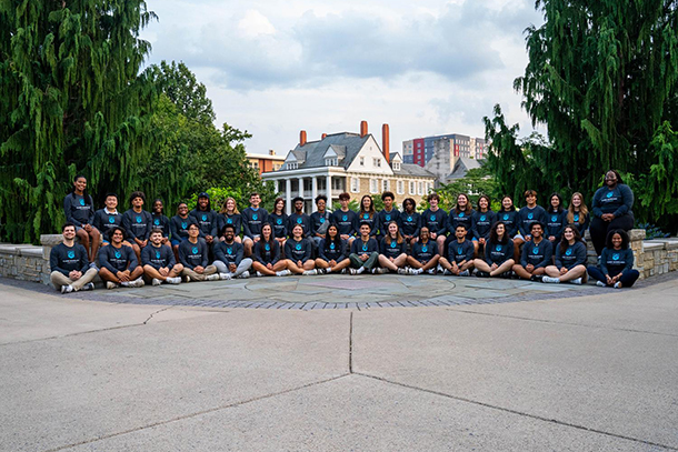 Thirty-nine people in matching t-shirts sit in two rows to pose for a photo outside.