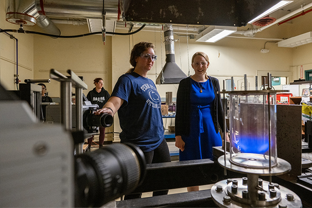 Jennifer Colborn and Jacqueline O’Connor stand in a laboratory, looking at a tube with a blue light in it