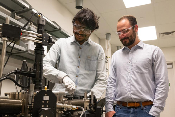 Two people in safety goggles operate equipment in a lab