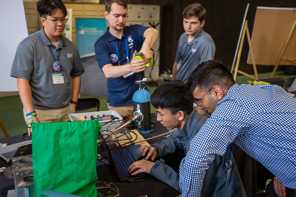 image of five students hovering over laptop and preparing various pieces of equipment.
