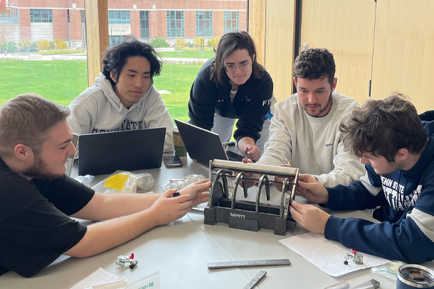 Five students gathered around a prototype on a table.