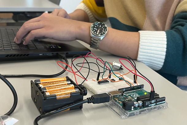 A hand types on a laptop keyboard next to an electrical device.