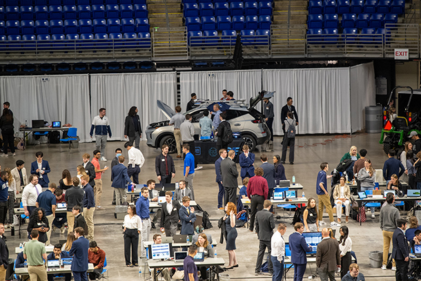 Students walk around tables and a car that are on the floor of the Bryce Jordan Center.