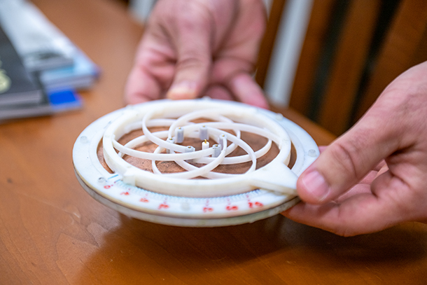 A small, circular, white and tan antenna prototype is displayed on a table