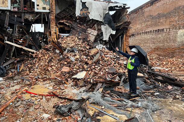 An individual looks toward and points at a large pile of building materials, bricks and rubble.