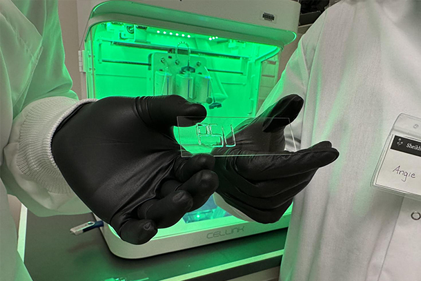 Two gloved hands hold a bioprinted granular hydrogel that spells "PSU."