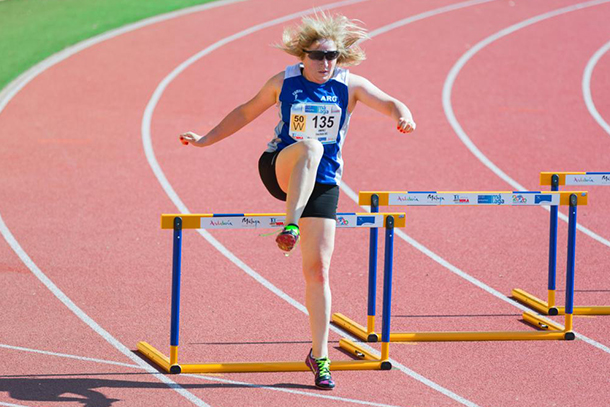 A runner jumps a hurdle on a track