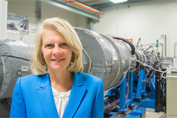 A person in a blue blazer smiles at the camera in front of a turbine in a lab