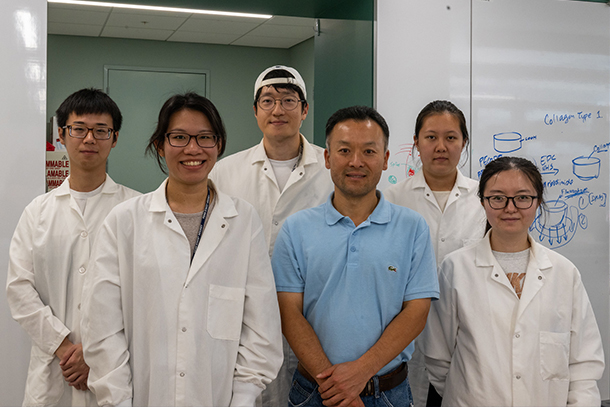 six people in a laboratory stand next to each other as they pose for a photo