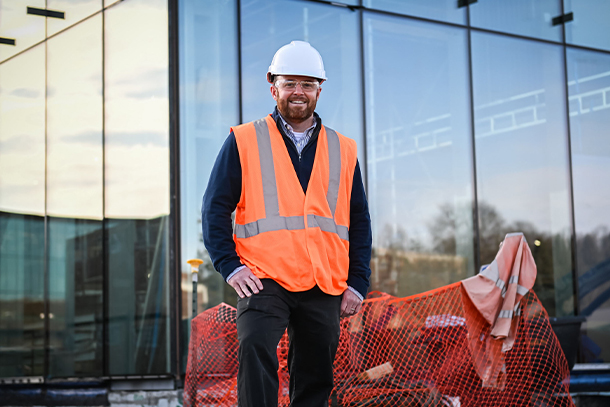 person in construction vest and hard hat poses for photo outside of building under construction