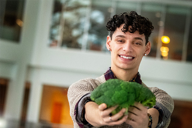 student holds up broccoli and smiles for photo