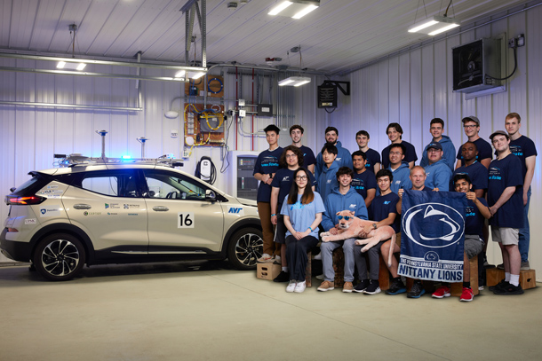 Students stand beside an autonomous vehicle parked in a garage. 