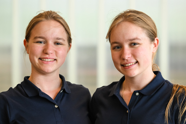 An indoors portrait of two individuals wearing blue polo shirts.