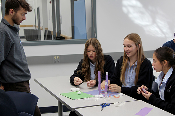 Three individuals seated at a table and one standing in front.