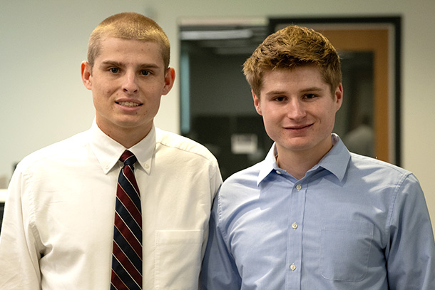 Two students wearing professional attire pose indoors.” class=