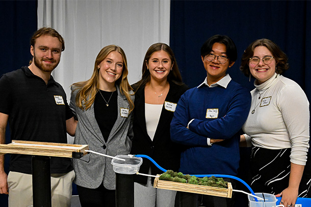 Students pose with an engineering project in a large event venue. 