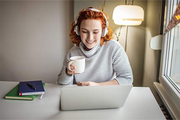 Person using a laptop and wireless headphones while working at home.