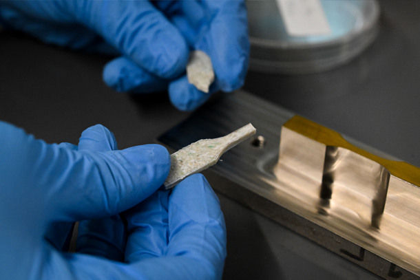 Gloved hands handle a composite sample of mixed plastics and ceramics.