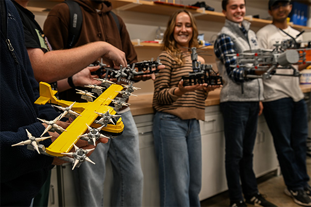 A group of students hold LEGO models of planes in a lab setting. 