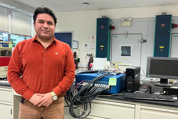 person smiles for photo while standing next to lab equipment