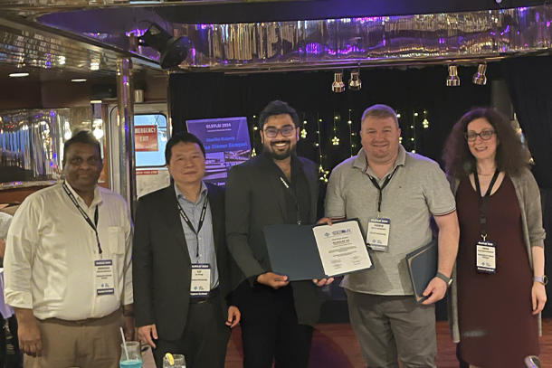 Five people pose for a photo while the person in the middle accepts an award.