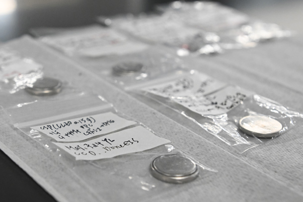 Coin cell battery samples are arranged in plastic bags on a lab table.